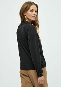 Sort langærmet top med en tætsiddende design og blød tekstur, med en høj krave og en glat bagsøm. Parret med beige bukser.