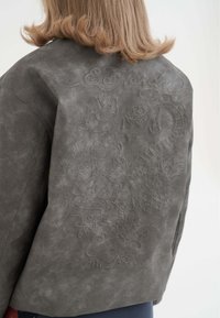 Giacca in suede grigia con design in rilievo di fiori e un drago sulla schiena, dalla vestibilità rilassata e finitura texturizzata.