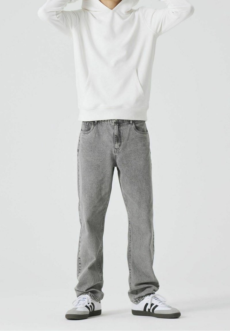 Sweat à capuche blanc, jean en denim gris, et chaussures de sport noires et blanches. Design simple, texture douce, et coupe droite.