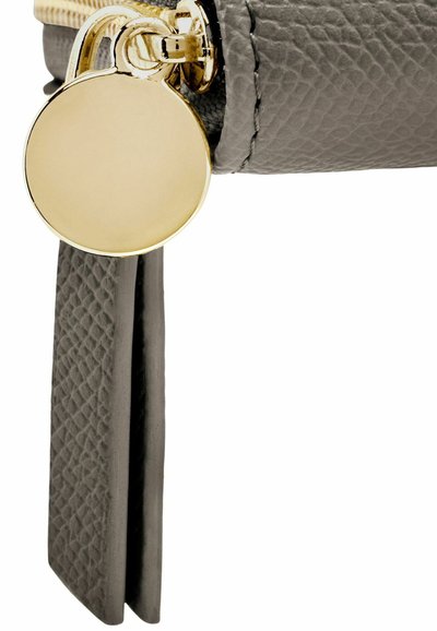 Tirette ronde en or attachée à une languette de fermeture éclair en cuir texturé gris sur un article en cuir gris.