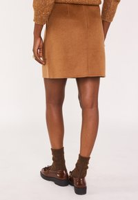 Jupe en laine marron au design épuré, avec des coutures latérales et un ourlet se terminant au-dessus du genou. Assortie à des chaussures marron foncé et des chaussettes texturées.