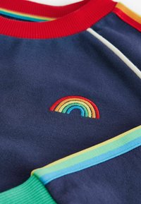 T-shirt di tessuto blu navy con una piccola ricamo arcobaleno. Collo a costine rosso e dettagli a strisce multicolori lungo le maniche.
