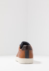 Braune Ledersneaker mit glatter Oberfläche, einem gepolsterten Kragen in Marineblau, weißer strukturierten Gummisohle und vertikalen schwarzen Akzenten an der Ferse.