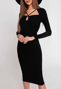 Donna che indossa un abito midi aderente nero a coste con maniche lunghe e un design a tracolla incrociata nel collo a quadrato.