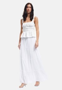Top bianco con peplum, spalline regolabili e texture a pieghe, abbinato a una lunga gonna bianca fluida con volant a strati.