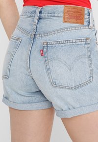 Vaaleansiniset farkkushortsit, joissa on korkea vyötärö, käännetyt lahkeet ja nahkainen takapatch, jossa on Levi Strauss -logo. Kaksi takataskua näkyvissä.
