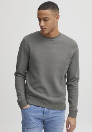 Gray waffle-knit sweatshirt with a round neckline and ribbed cuffs. Paired with light blue jeans, featuring a relaxed fit and subtle distressing.