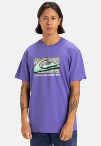 Camiseta de manga corta morada con un diseño gráfico de una ola y el texto "Quiksilver" en la parte frontal. Hecha de suave tejido de algodón.