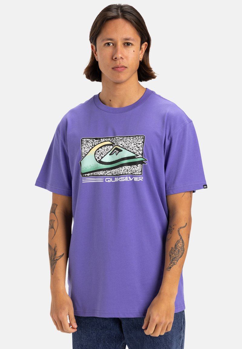 Camiseta de manga corta morada con un diseño gráfico de una ola y el texto "Quiksilver" en la parte frontal. Hecha de suave tejido de algodón.