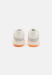 Zapatillas grises y blancas con suelas naranjas, que cuentan con un panel trasero texturizado y acentos de malla, diseñadas con un silueta de corte bajo.