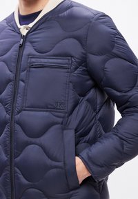 Μπλε σκούρο καπιτονέ μπουφάν με φερμουάρ μπροστά, με τσέπη με φερμουάρ στο στήθος και λογότυπο CK στο πλάι. Λεία, επενδυμένη υφή.