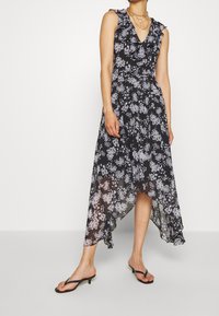 Black floral dress with a ruffled neckline, asymmetrical hem, and sheer fabric. Styled with black sandals, featuring fine straps.