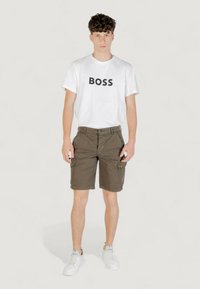 T-shirt bianco da uomo in cotone con la scritta "BOSS" stampata in nero, abbinato a pantaloni cargo verde oliva con più tasche e un design aderente.