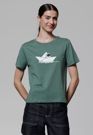 T-shirt en coton vert avec un motif d'un bateau en papier et un astronaute. Manches courtes, col rond et coupe décontractée.