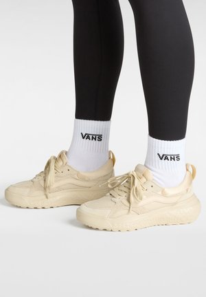 Sneakers beige realizzati in mesh e materiali sintetici, con suola testurizzata, chiusura con lacci e collo imbottito, indossati con calze bianche Vans.