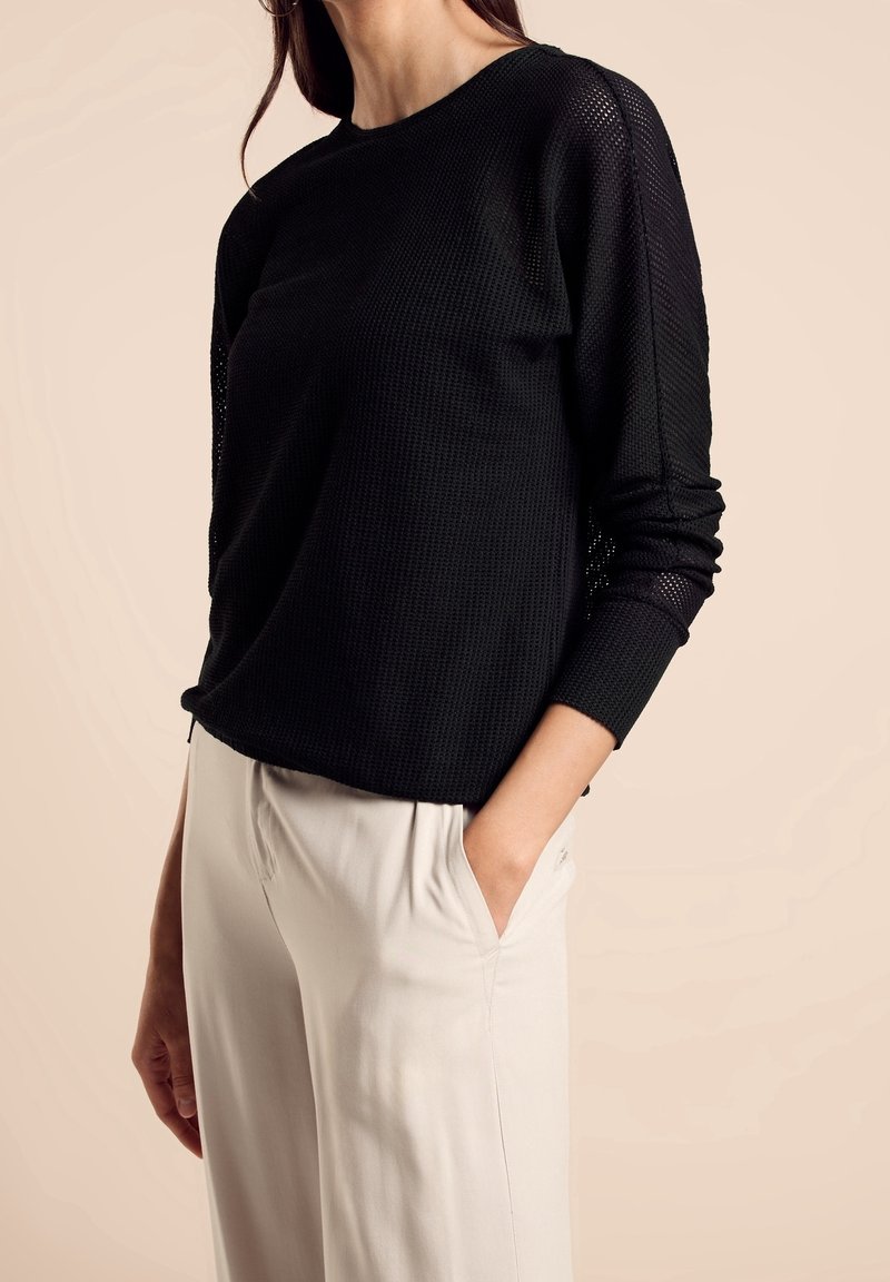 Suéter negro de punto waffle con mangas largas, escote redondo y diseño texturizado. Combinado con pantalones de tiro alto en beige claro.