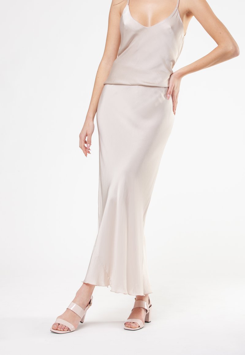 Silke camisole og lang nederdel sæt i lys beige, med et flydende design og en blød tekstur. Pink hæle sandaler med ankelstropper.