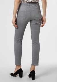 Jeans ajustados grises de mezclilla, con una cintura de altura media, bolsillos traseros con detalles de costura sutil, combinados con zapatos de tacón de bloque negros.