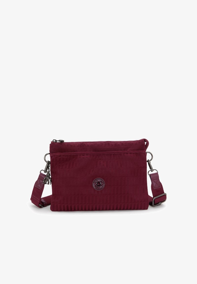 Borsa a tracolla color bordeaux in tessuto testurizzato, con chiusura a zip e tracolla regolabile. Presenta un emblema del logo sulla parte anteriore. Forma compatta e rettangolare.