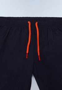 Tamsiai mėlynos šortai su elastinga juostele ir oranžiniais raišteliais. Lengvas audinys su šiek tiek susiraukšlėjusia tekstūra.