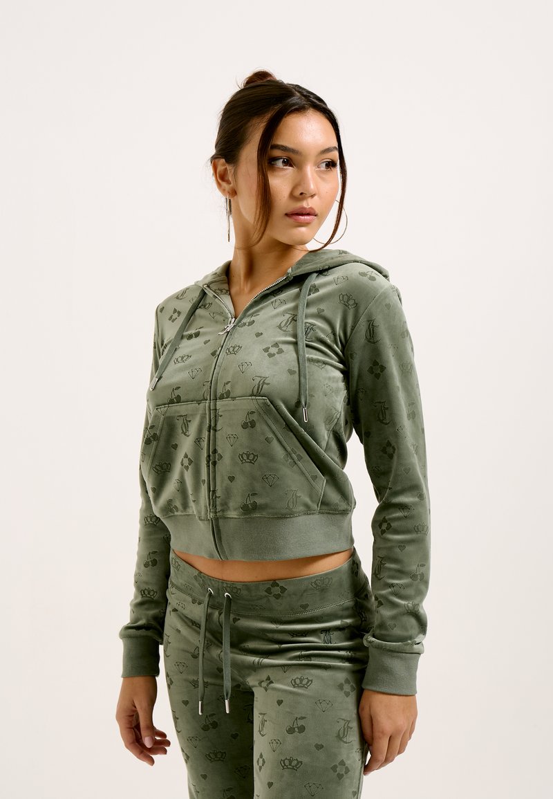 Green velour zip-up hoodie with drawstrings, featuring a front pocket and subtle brand logo patterns. Paired with matching jogger pants.