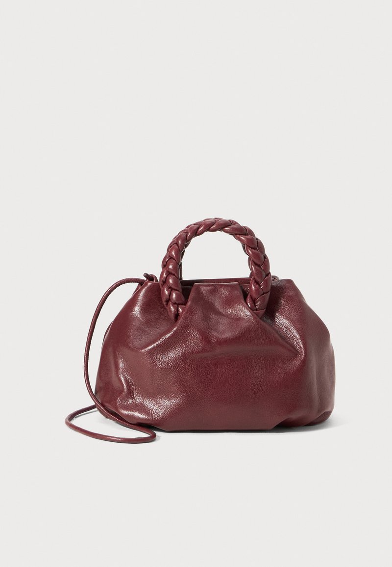 Burgundy leather handbag with a braided handle, soft texture, and a rounded shape. Features a removable shoulder strap for versatility.