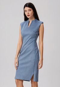 Robe sans manches bleue avec un col haut, dotée d'une fente latérale et d'une texture lisse et douce. La coupe ajustée met en valeur les contours du corps.