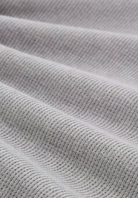 Textil in hellgrau mit einem strukturierten, gerippten Muster. Weiches, flexibles Material mit sichtbaren wellenförmigen Linien und kleinen Farbtupfern.