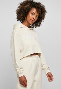 Sweat à capuche beige raccourci avec un logo "STARTER" blanc sur le devant, avec une capuche à cordon de serrage et des poignets élastiques, assorti avec un pantalon de jogging.