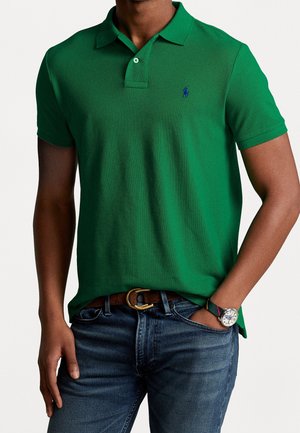 Groen poloshirt van gestructureerde stof, met een kraag, geborduurd logo en korte mouwen, gecombineerd met een blauwe spijkerbroek en een horloge.