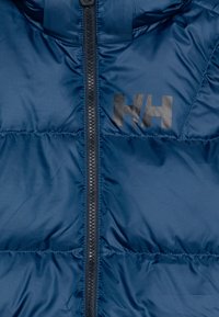 Chaqueta aislante en color azul marino con cremallera frontal, textura suave, secciones cosidas y un logo negro en el pecho.