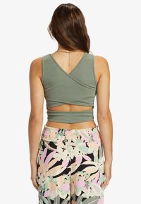 Oliivinvihreä lyhyt tank top, jossa on teksturoitu kuvio ja V-mallinen takaosa; yhdistettynä kukkakuosiset housut vaaleanpunaisena, vihreänä ja mustana.