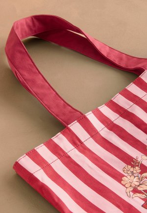 Borsa tote in tela con strisce rosse e bianche, con un motivo floreale su un lato e manici spessi in tessuto rosa. Texture liscia.