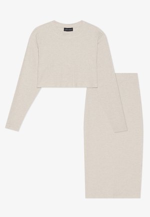 Lichtbeige geribbelde tweedelige set bestaande uit een cropped longsleeve top en een knie-lange rok, beide gemaakt van textuur gebreide stof.