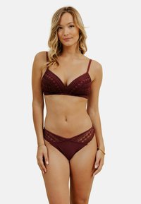 Ensemble de lingerie bordeaux comprenant un bralette en dentelle en forme de triangle et un bas de bikini assorti avec des accents en dentelle diagonale. Texture douce.