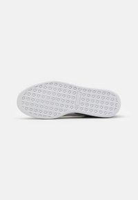 Semelle de chaussure blanche avec une texture antidérapante, présentant un motif géométrique. Bords arrondis lisses et un détail de couleur contrastante sur le côté.