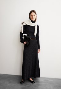 Schwarzes, geripptes Strickkleid mit langen Ärmeln, strukturiertem Stoff und taillierter Passform. Kombiniert mit einem hellgrauen Schal und schwarzen Accessoires.