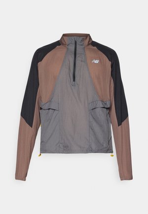 Viegls puszipa jaka ar brūniem un pelēkiem paneļiem, melnām piedurknēm, ar rāvējslēdzēju kabatām un regulējamu apakšmali. Redzams New Balance logs.