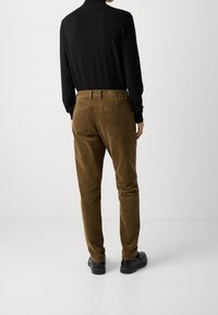 Brown corduroy pants with a slim fit, featuring back pockets and a waistband. Paired with a fitted black long-sleeve top and black shoes.