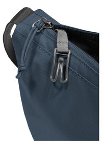 Gros plan d'un coin de sac en tissu bleu avec une fermeture éclair partiellement ouverte et une boucle élastique grise attachée à une sangle près du curseur de la fermeture éclair.