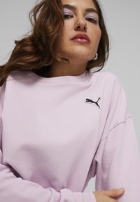 Hele roosa sweatsiit, millel on ümmargune kaelus, must Puma logo rinnal ja pikad varrukad. Pehme, tekstureeritud kangas.