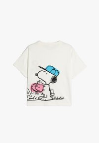 Camiseta de algodón blanca con un gráfico de Snoopy con una gorra azul sosteniendo un objeto rosa, con detalles contorneados en negro y un corte holgado.