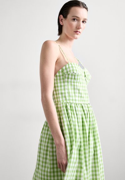 Groene gingham jurk met een aansluitend lijfje, dunne bandjes en een uitlopende rok. Vervaardigd van een geweven katoen stof met witte ruitpatronen.