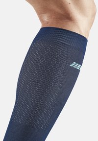 Kompressionswadenmuff in Marineblau, mit strukturiertem Stoff und einem Farbverlaufsmuster sowie einem kleinen Logo in Hellblau.