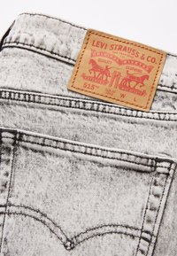 Grå denimjeans med en läderetikett som visar "Levi Strauss & Co." och en grafisk design. Har distinkta sömmar och en tapered fit-design.