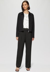 Veste noire courte avec col, associée à un haut blanc à motif cœur et un pantalon noir taille haute. Sandales à orteils carrés.