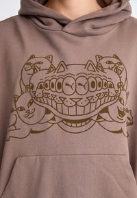 Brun hættetrøje med et grafisk design af smilende katte og et stort tandfyldt ansigt. Blødt materiale med en frontlomme og hætte med snørebånd.
