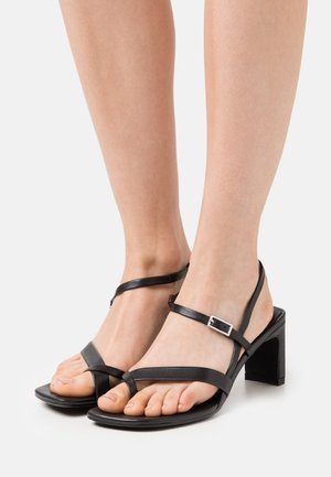 Sandalias de cuero negras con diseño de tiras, tacones cuadrados y una correa en el tobillo con un detalle de hebilla de metal. Textura suave y punta descubierta.