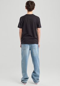 Black cotton t-shirt with short sleeves paired with light blue denim pants featuring a slightly faded texture and back pockets.