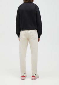 Černá mikina s dlouhým rukávem a raglánovými rukávy, doplněná o světlé béžové kalhoty rovného střihu a vícebarevné tenisky.